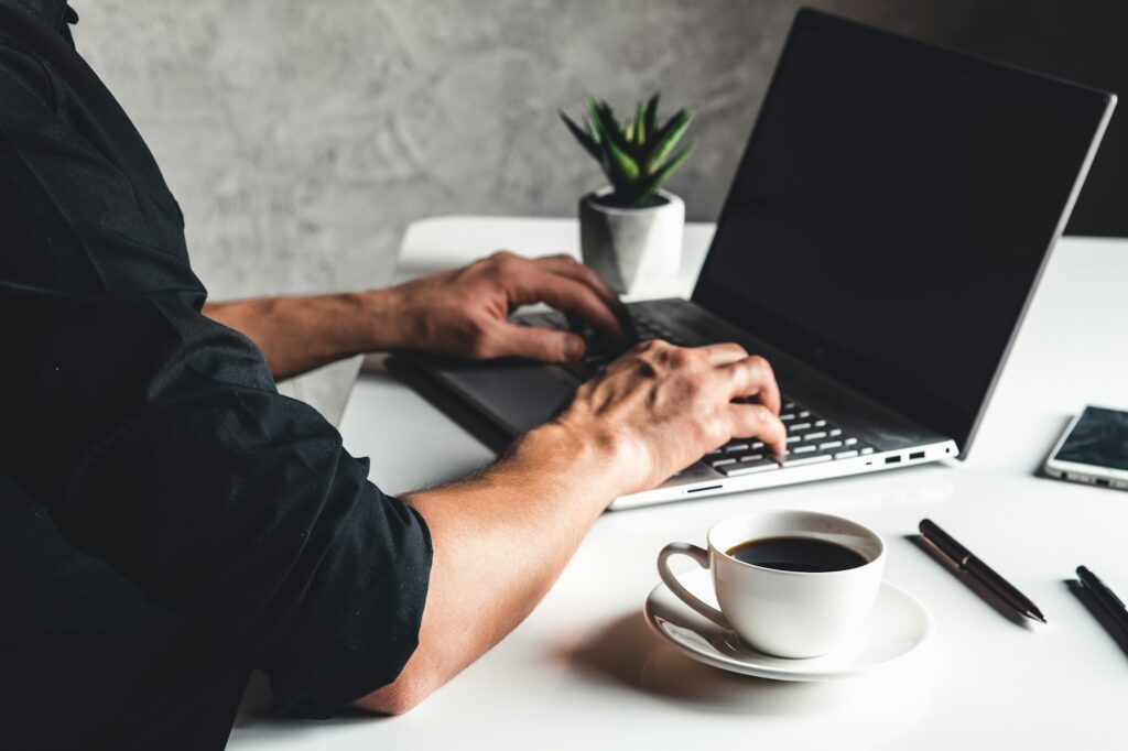 A man types on a laptop, business concept, glasses, a cup of coffee and a pen on a gray background.